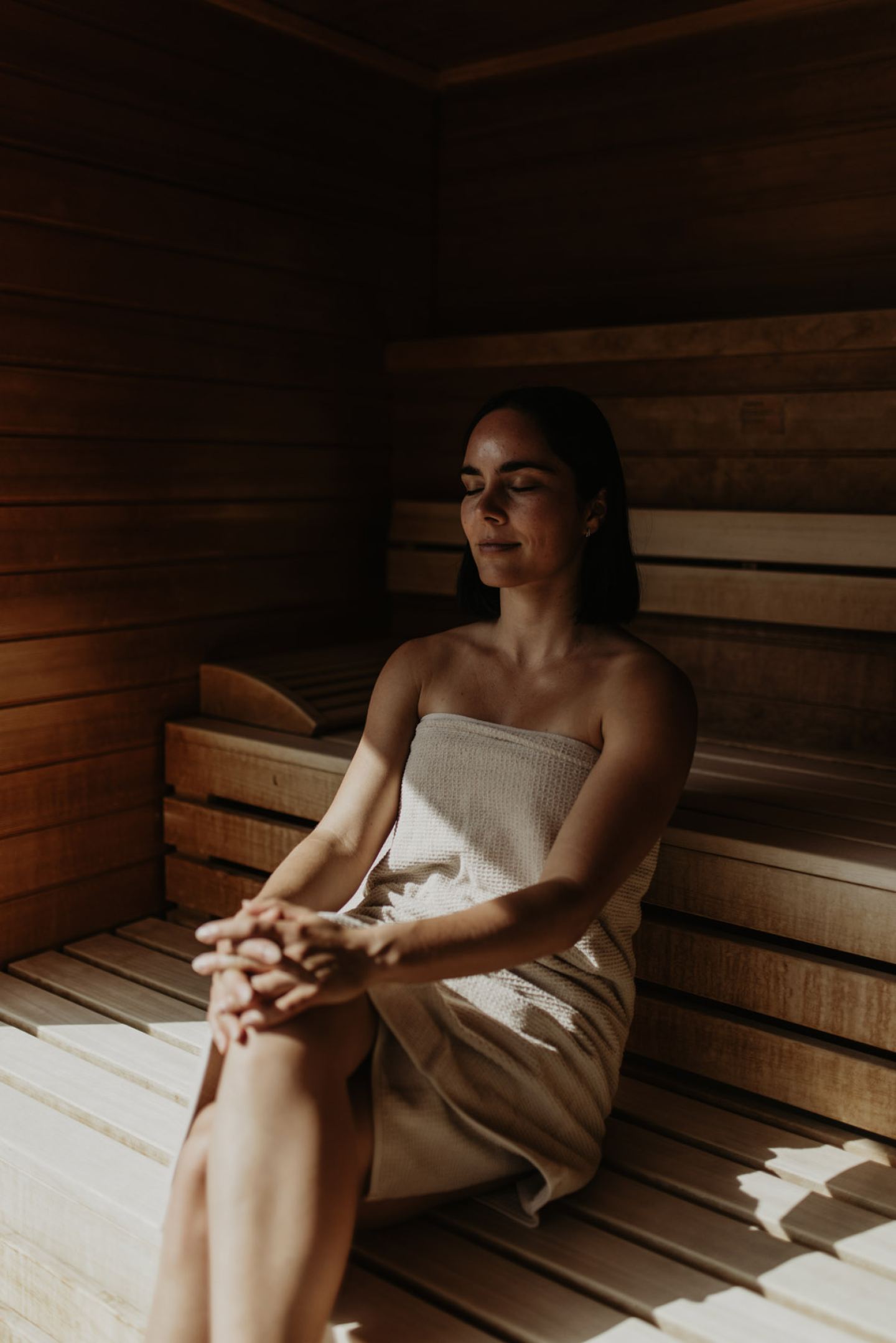 Frau mit geschlossenen Augen entspannt in der Sauna, von Sonnenlicht gestreift