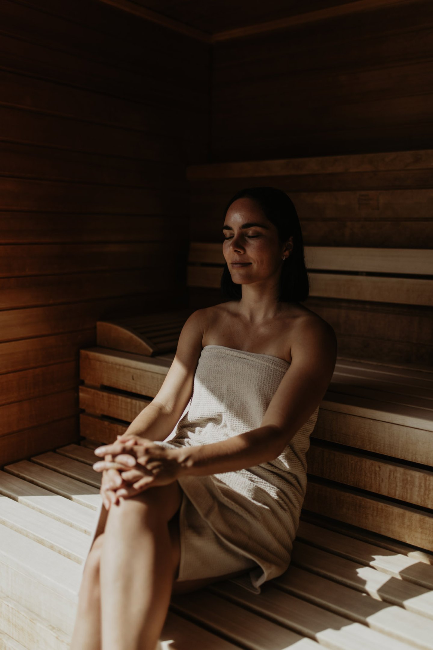 Frau mit geschlossenen Augen entspannt in der Sauna, von Sonnenlicht gestreift