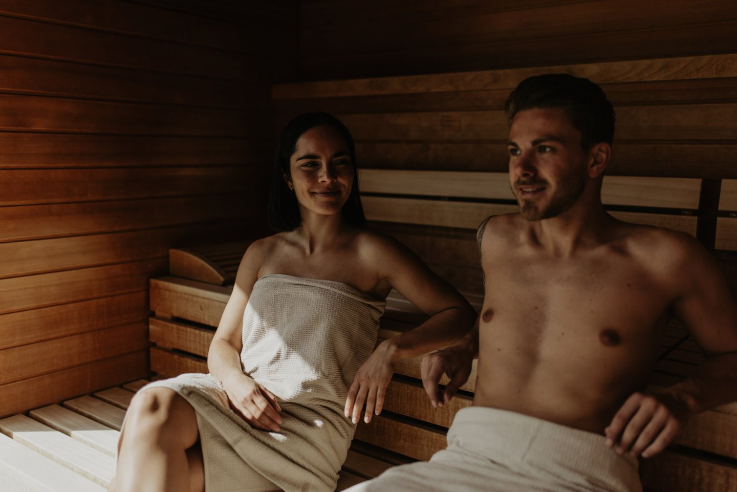 Paar in Handtüchern sitzt entspannt nebeneinander in der Sauna aus hellem Holz