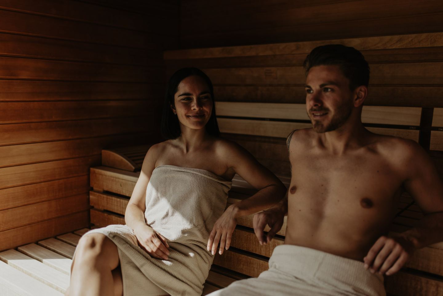 Paar in Handtüchern sitzt entspannt nebeneinander in der Sauna aus hellem Holz
