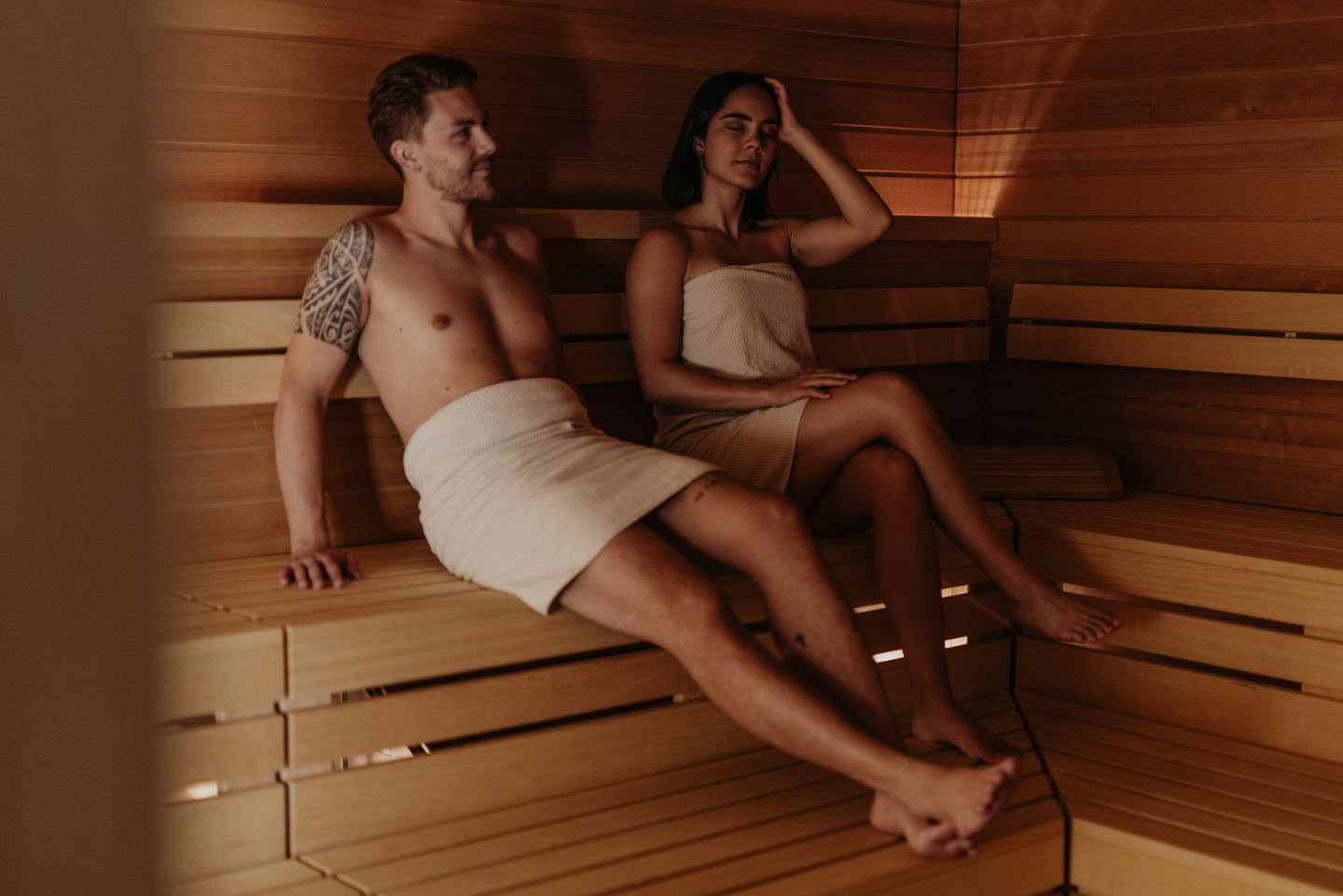 Couple in towels sitting relaxed in the light-wood sauna