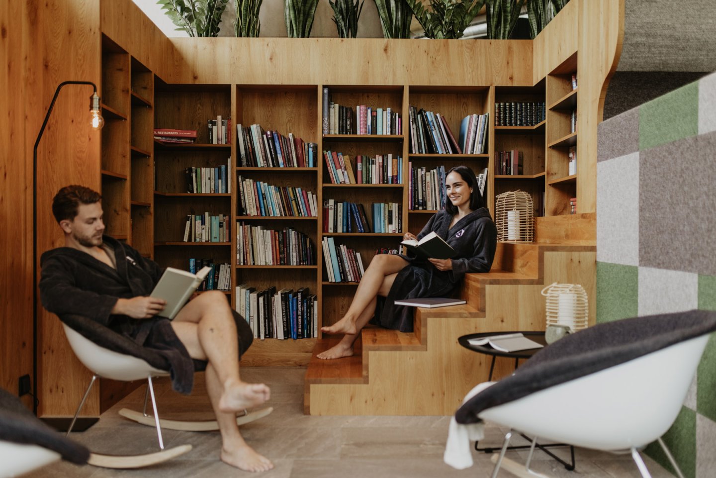 Leseecke mit hoher Bücherwand aus Holz, zwei Gäste in Bademänteln lesen