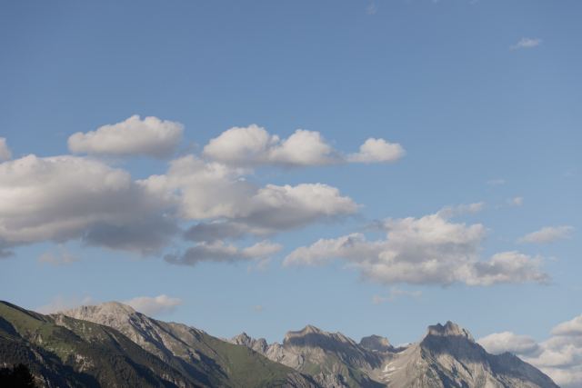 Mountain ridge with rugged peaks and fluffy clouds above green slopes