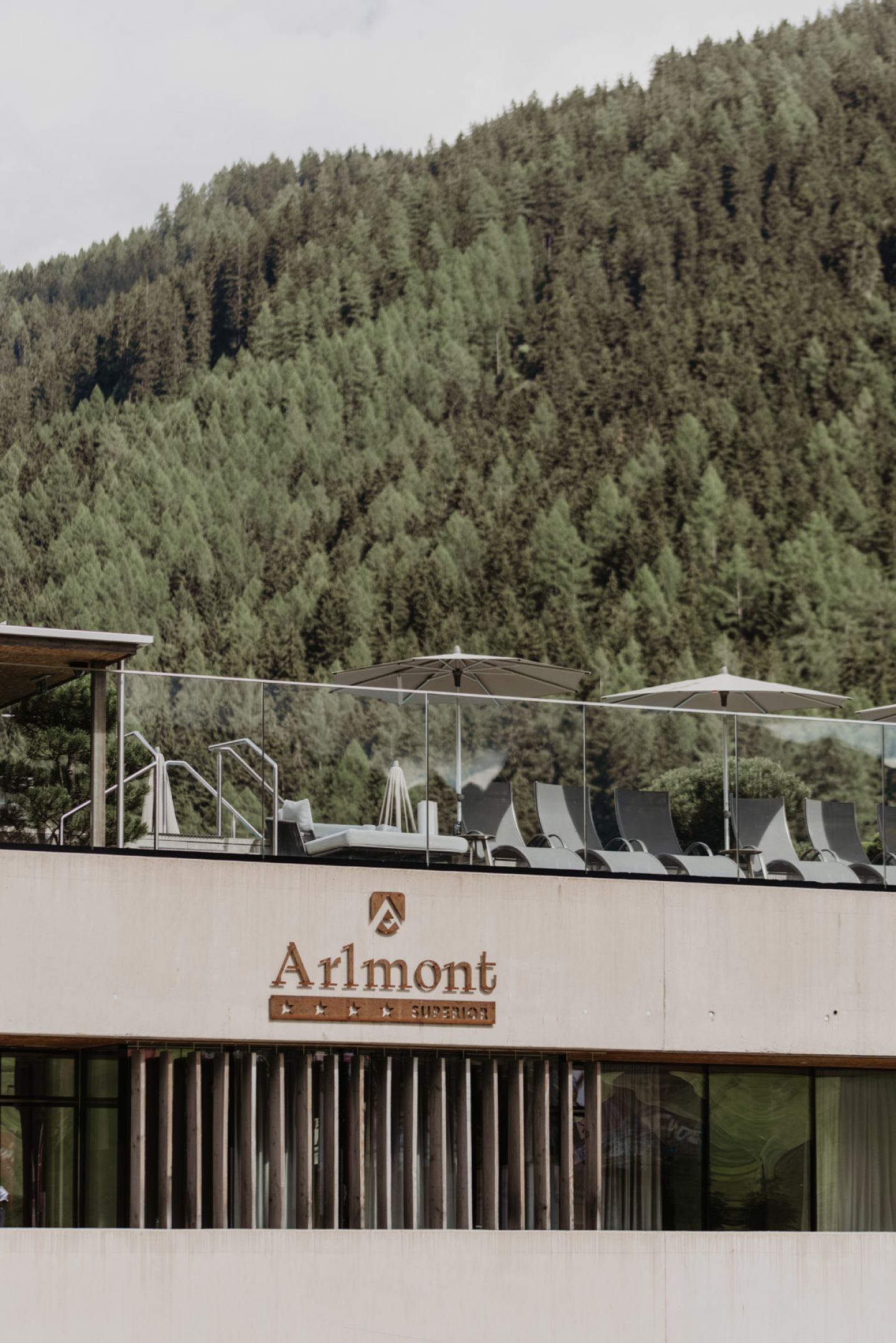 Sun terrace with loungers and parasols above the façade, with a wooded mountainside behind