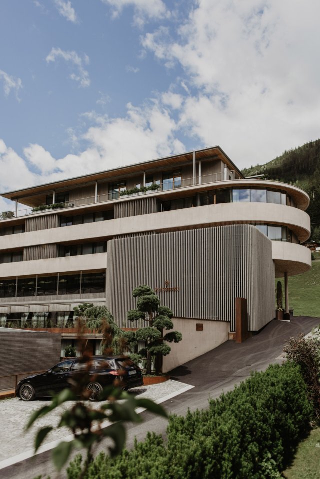 Das geschwungene Gebäude aus Sichtbeton und Holzlamellen mit Zufahrt und geschnittenen Formgehölzen