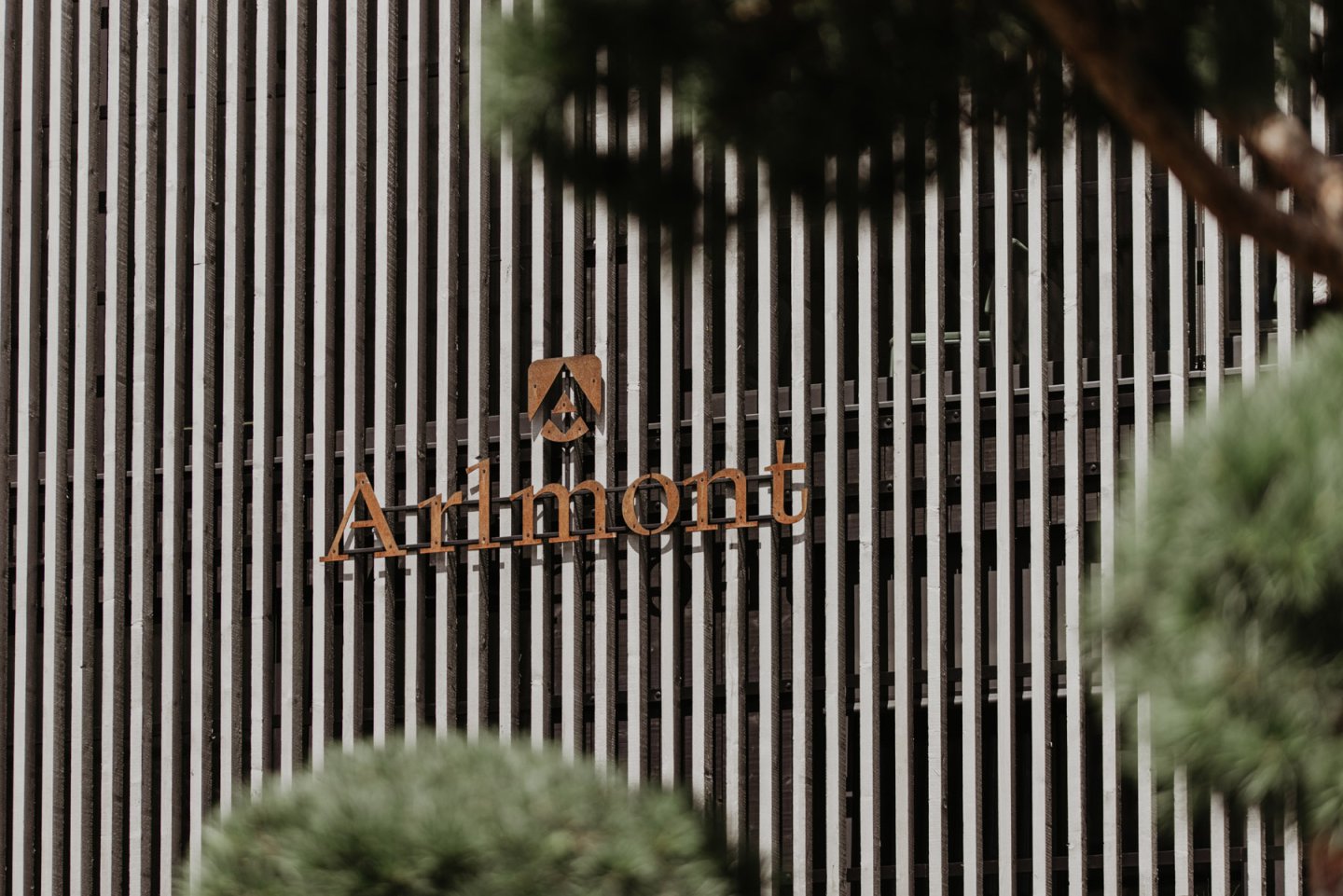 Der Arlmont-Schriftzug aus Cortenstahl an der Fassade aus Holzlamellen