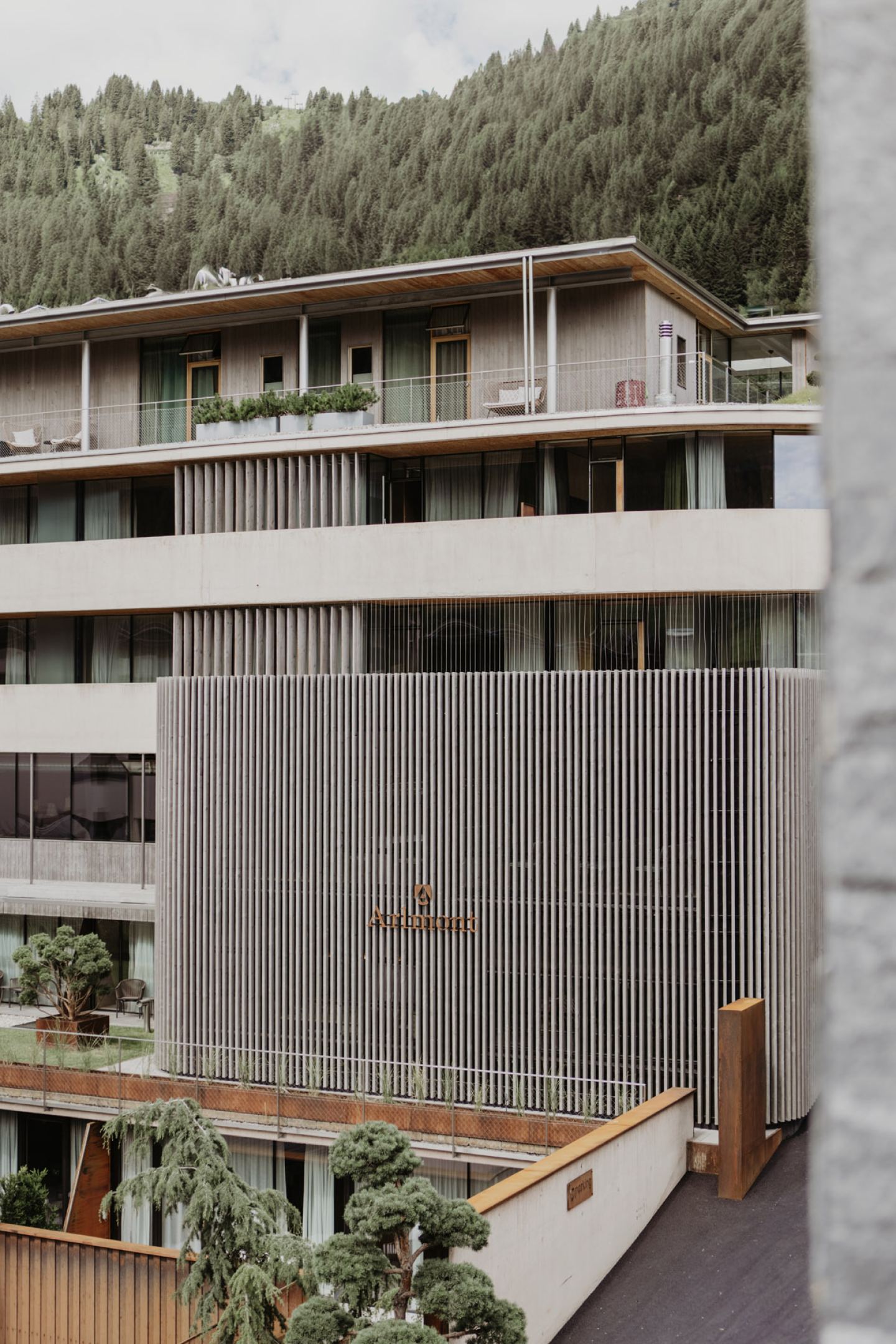 Fassade mit dem Schriftzug und begrünten Terrassen, unten die Café-Terrasse mit Stühlen