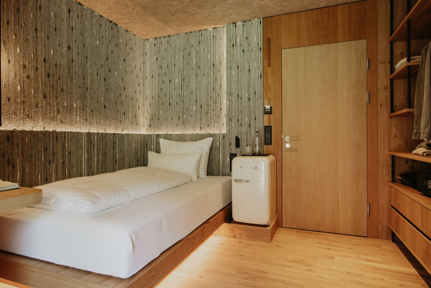 Einzelzimmer mit Bett an der gewebten Wand, SMEG-Minibar und offener Garderobe