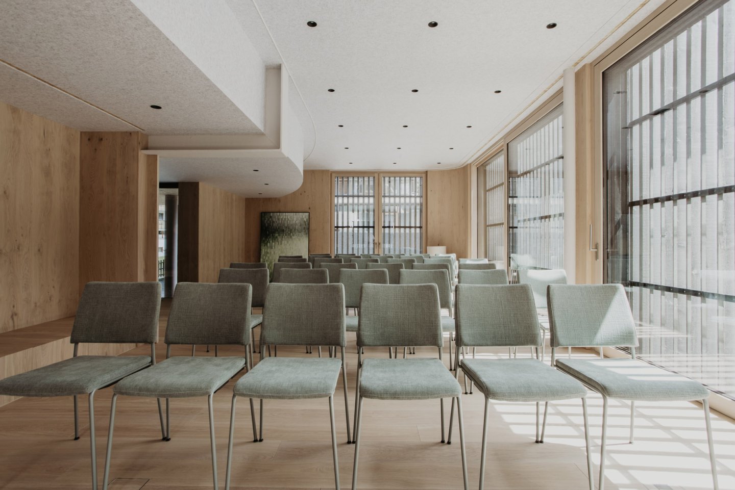 Konferenzraum mit Reihenbestuhlung aus grünen Stühlen vor der holzverkleideten Wand