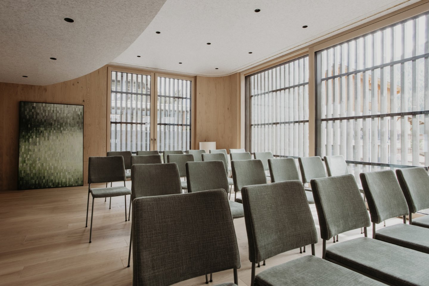 Konferenzraum mit grünen Stühlen in Reihen und einem grünen Kunstwerk an der Wand