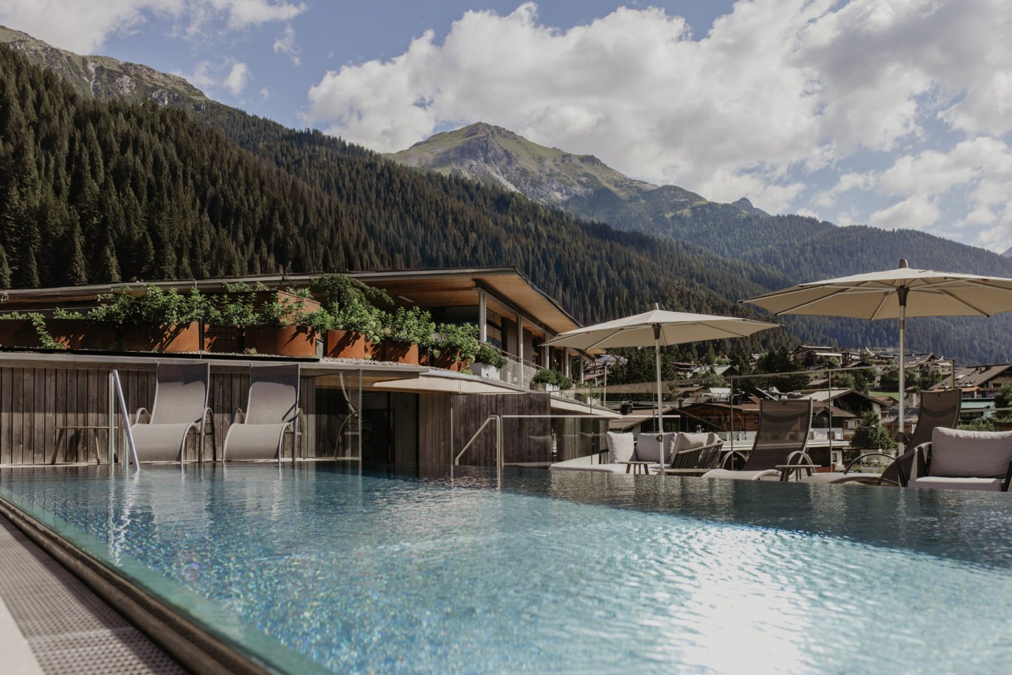 Rooftop Pool mit Liegen vor der Holzfassade, dahinter das Bergpanorama