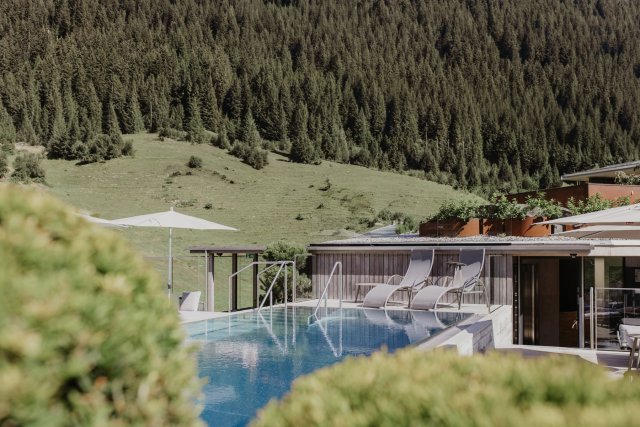 Rooftop Pool mit Liegen entlang der Holzfassade, dahinter eine grüne Bergwiese