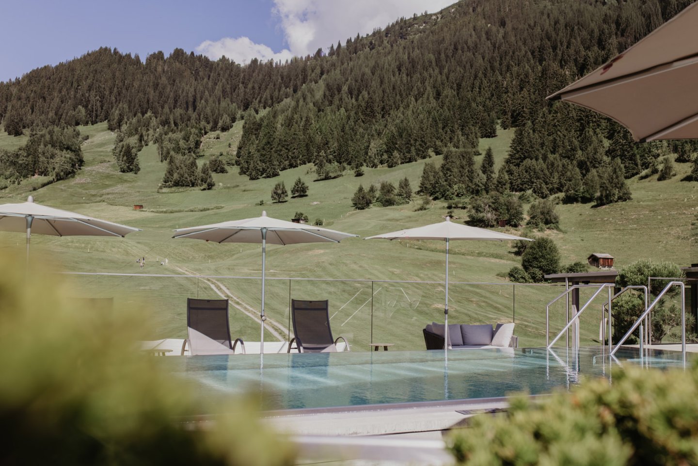 Rooftop Pool mit Sonnenschirmen und Liegen, dahinter die Wiese des Golfplatzes