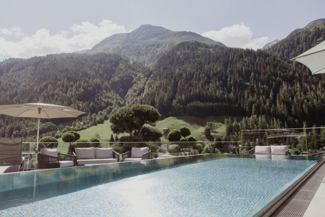 Rooftop Pool mit Loungemöbeln und Sonnenschirmen vor dem Bergpanorama im Sommer