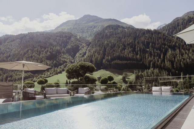 Rooftop Pool mit Loungemöbeln und Sonnenschirmen vor dem Bergpanorama im Sommer